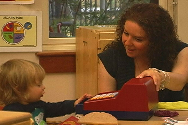 A teacher and toddler play with a cash register.