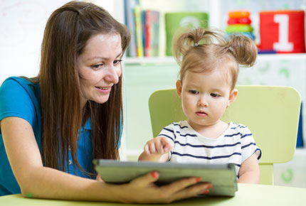 Adult assists toddler with tablet device