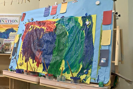 A double easel with a large sheet of paper covered in colorful paint