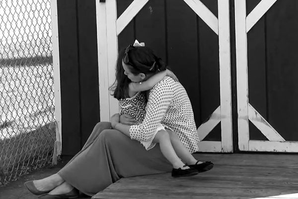 A teacher sits on the ground hugging a child in her lap. 