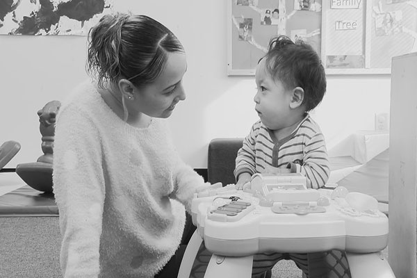 A teacher looks at and talks to a toddler.