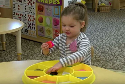 Child sorts colorful buttons on a tray. 