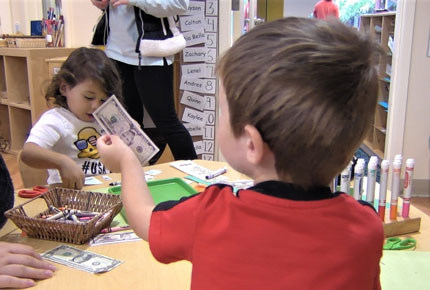 Preschooler sits at a learning center and holds a $5 bill