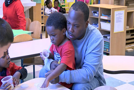 A teacher sits with a child in his lap, talking to him. 