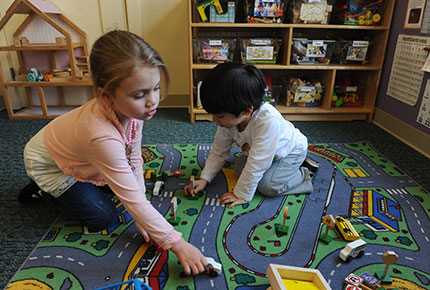 Children playing on the floor with wooden cars.