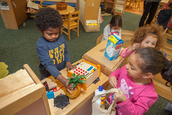 Children pretending to buy items with a wooden cash register. 