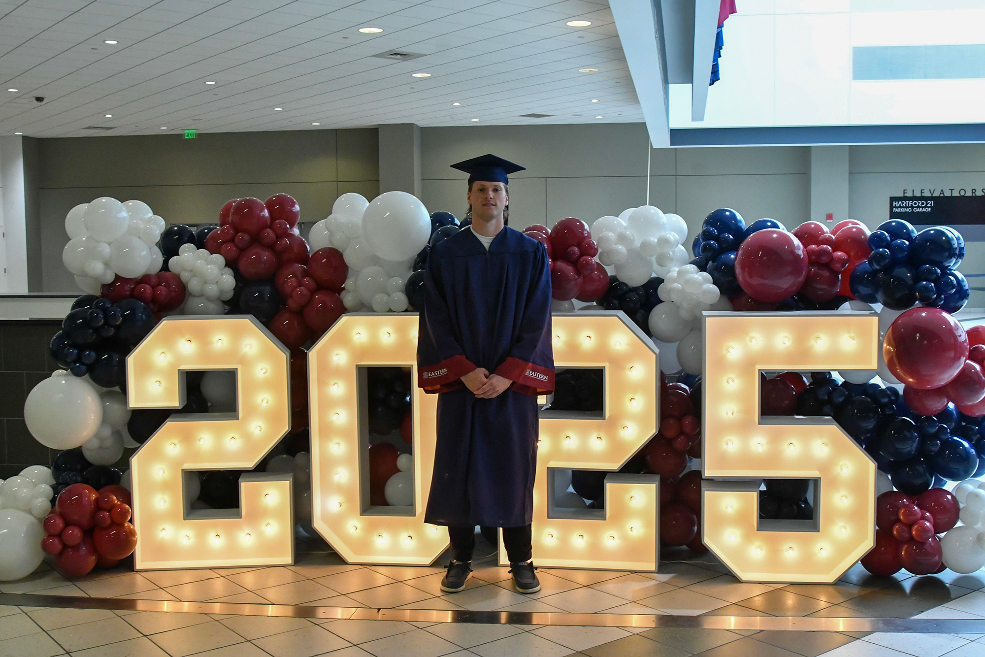 Student standing in front of large 2025 numbers dressed in graduation cap and gown