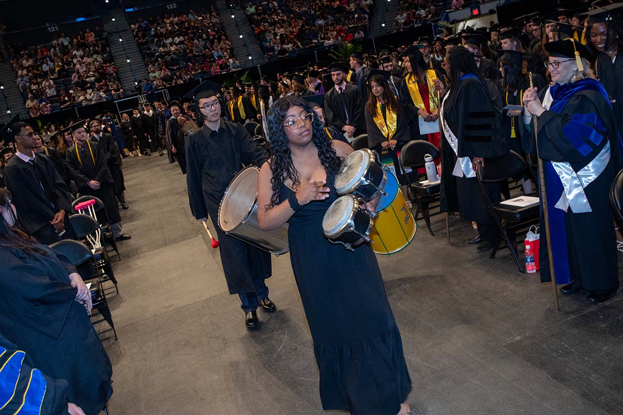 graduates play percussion instruments as they walk down the center aisle