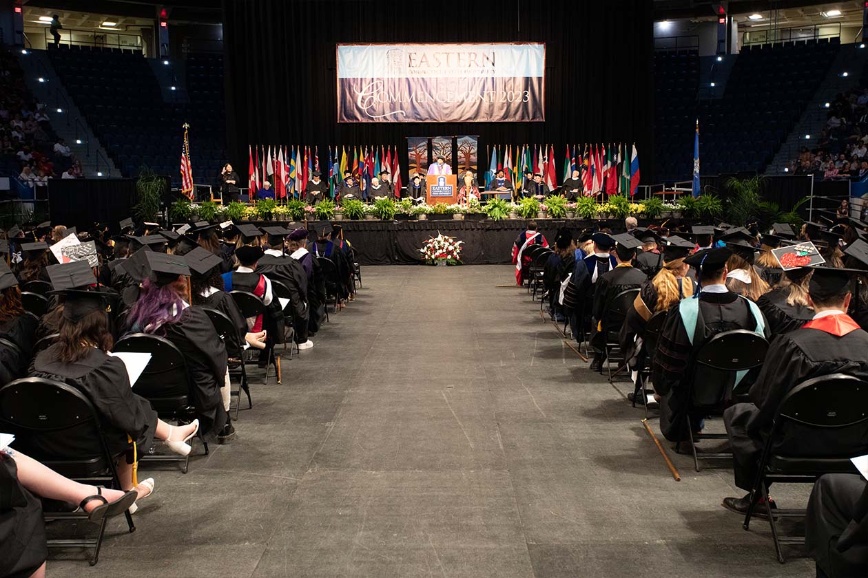 a view down the aisle, students to both sides, with the main stage and the Commencement 2023 banner at the far end