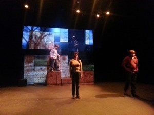 two student actors standing in the foreground while other student actors stand on elevated platforms behind them
