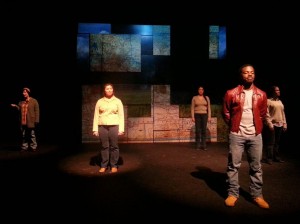 student actors standing at various points on the stage with spotlights on them