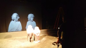 student actors brightly lit on the state with a projected image behind them