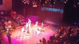 student actors sitting in a circle with the words "letting go" projected on the backdrop