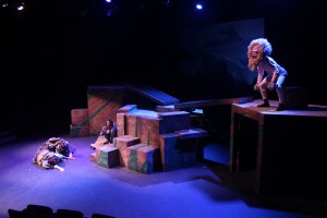 student actor in a beastly costume posted on top of a higher area of the stage while three others hide on the lower area