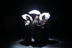 student actors holding umbrellas while under a stagelight