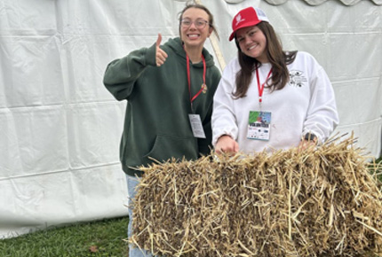 students posing for photo behind a hay bale