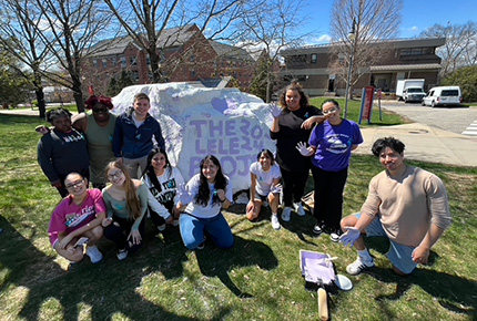 student posing for photo in front of a large decorated rock
