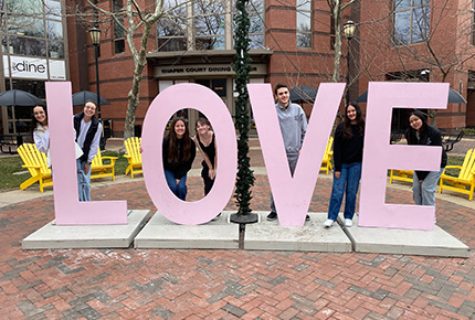 students standing around a large installation of the world Love in pink letters
