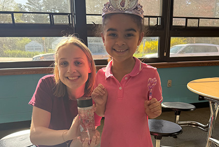 student holding a glittery water bottle and a child wearing a tiara and holding a pipe cleaner wand