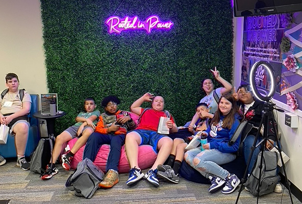 students posing for photo in front of neon Rooted in Power sign and green backdrop