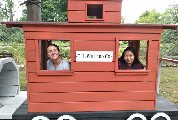 students sitting inside a small decorational train car with a sign for O.L. Willard Co. on the side