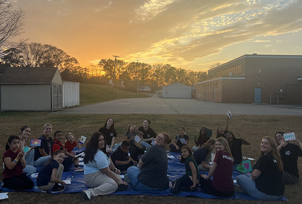 student sitting on a tarp on the grass while the sun sets in the background