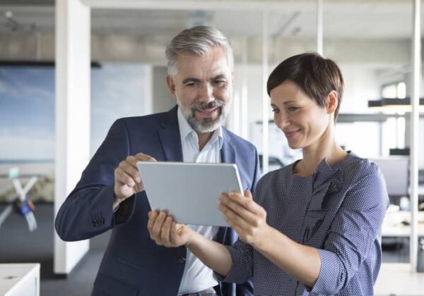 A businessman and businesswoman look together at a tablet in an office.