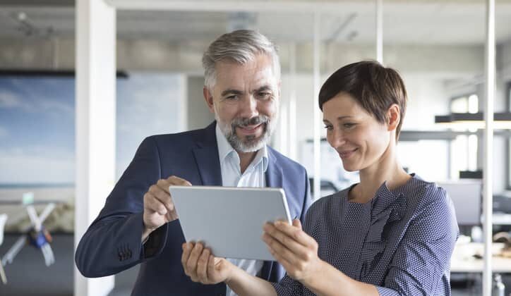 A businessman and businesswoman look together at a tablet in an office.