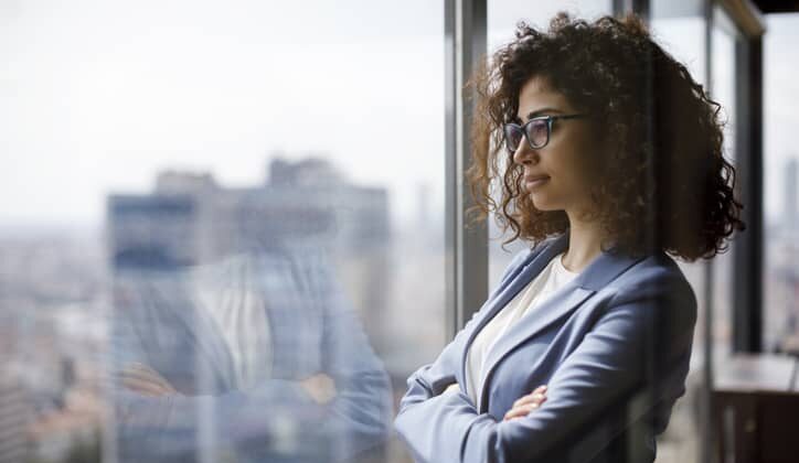 Woman manager looks through a glass window while standing in her office.