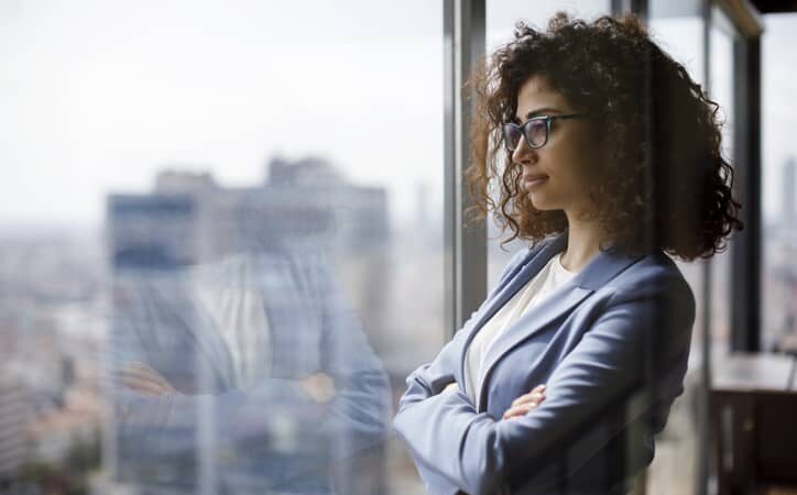 Woman manager looks through a glass window while standing in her office.