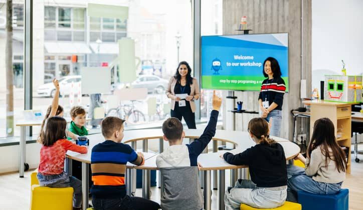 Children raise their hands to ask questions in a classroom.