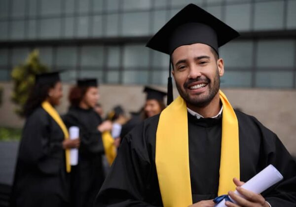 A happy male graduate student holding his diploma on graduation day.