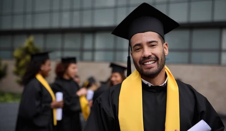 A happy male graduate student holding his diploma on graduation day.