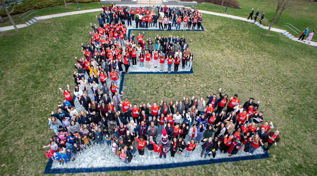 President Ismaili, Willi the Warrior, guests from the Inauguration and Eastern students posing for a photo on a gigantic, stenciled E