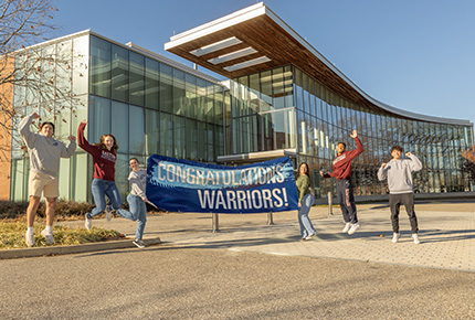 students cheering holding a Congratulations Warriors! banner