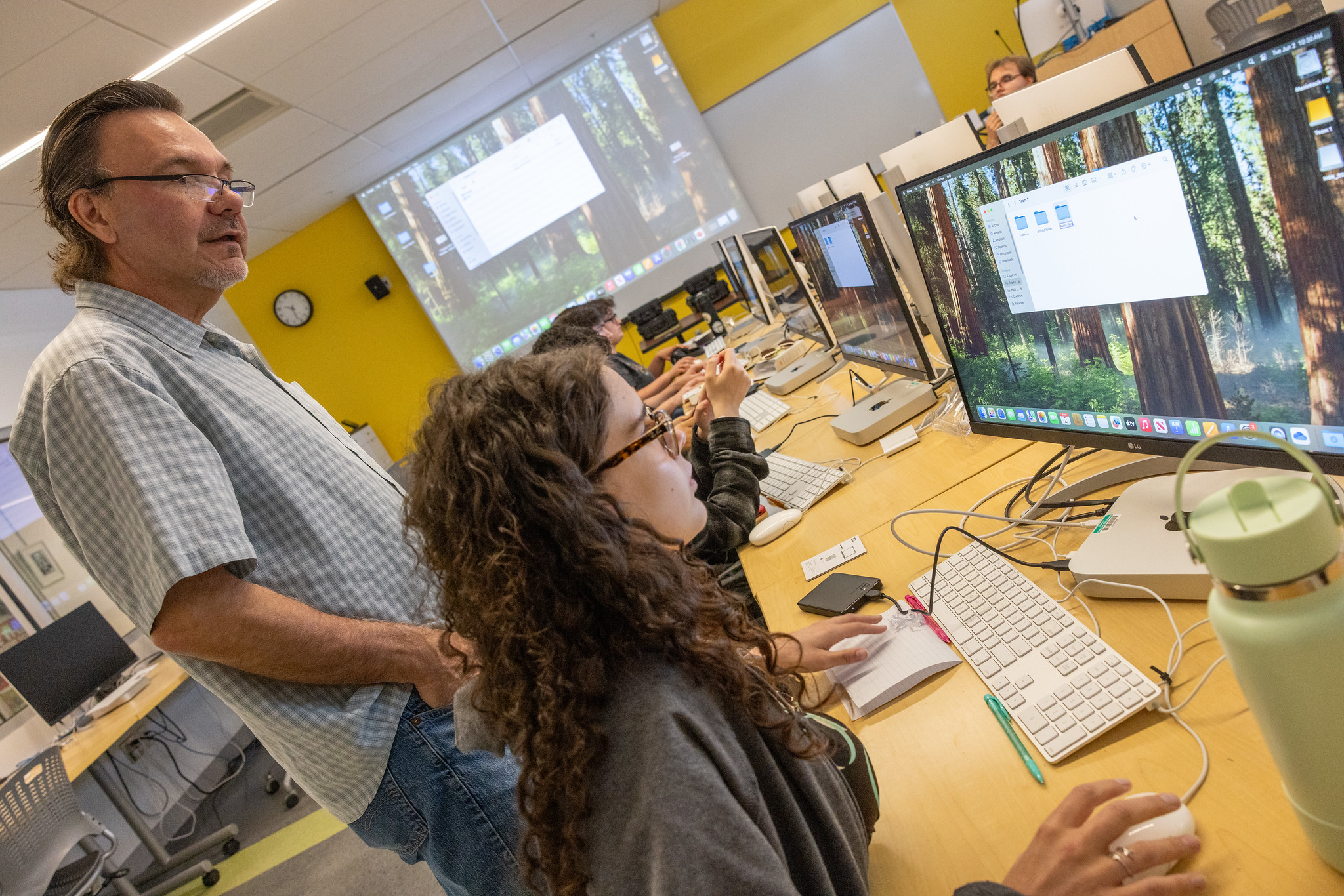 Professor guiding students at workstations in a new media lab