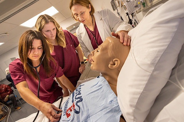 nursing students and professor using training dummy