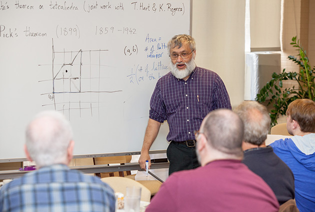 professor in front of a white board explaining a graphed diagram