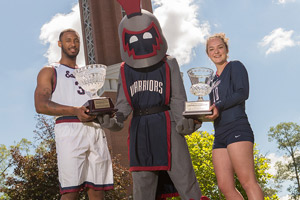 Men’s basketball player Tarchee Brown ’18 and women’s volleyball player McKenzie Maneggia ’20 pose with Willi the Warrior and the two LEC Cups