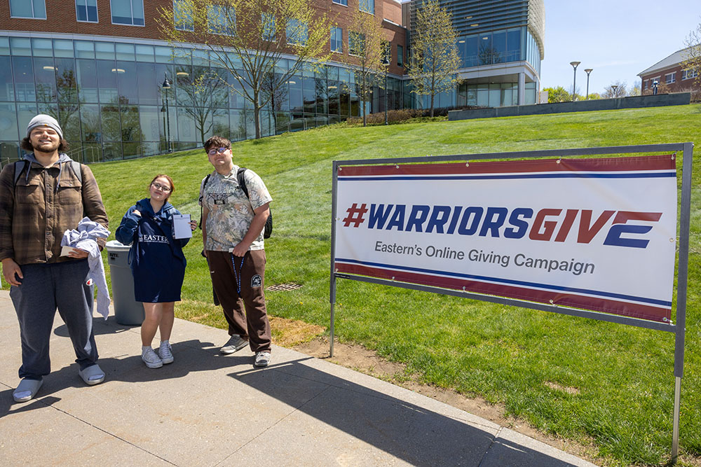 Students pose next to a Warriors Give sign at the Fine Arts Instructional Center Amphitheater.