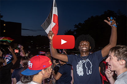 A group of students celebrating together, one holding a flag.
