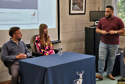 student giving a presentation as two representatives from The Hartford sit behind a table