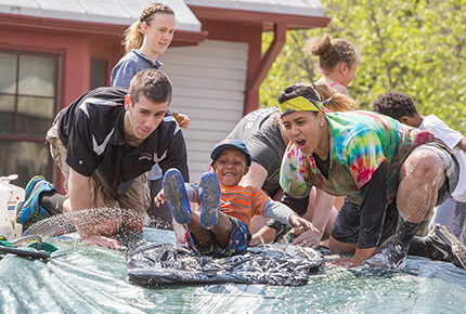 Students encouraging a child going down a water slide