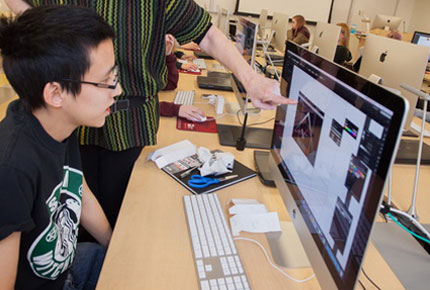 Student working on computer with professor overseeing